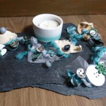 Schiefertafel mit einem Keramikeinsatz für ein Teelicht und verschiedenen Beiwerk dekoriert.